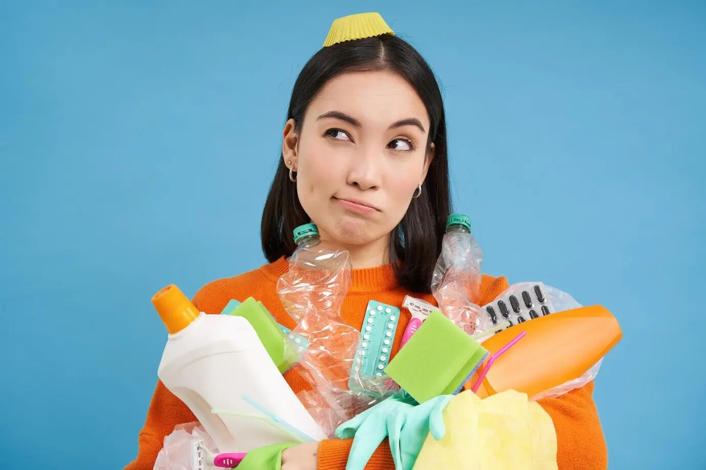 Portrait of an Asian woman with empty plastic bottles, looking to the side with a thoughtful expression, recycling garbage at